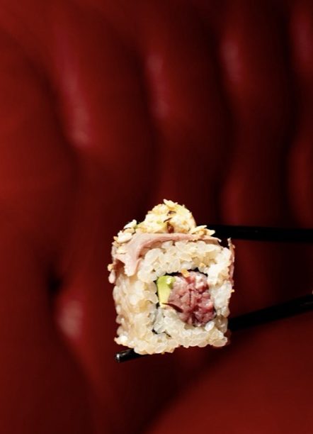 Uramaki di manzo tra le bacchette, davanti a un divano rosso capitonné